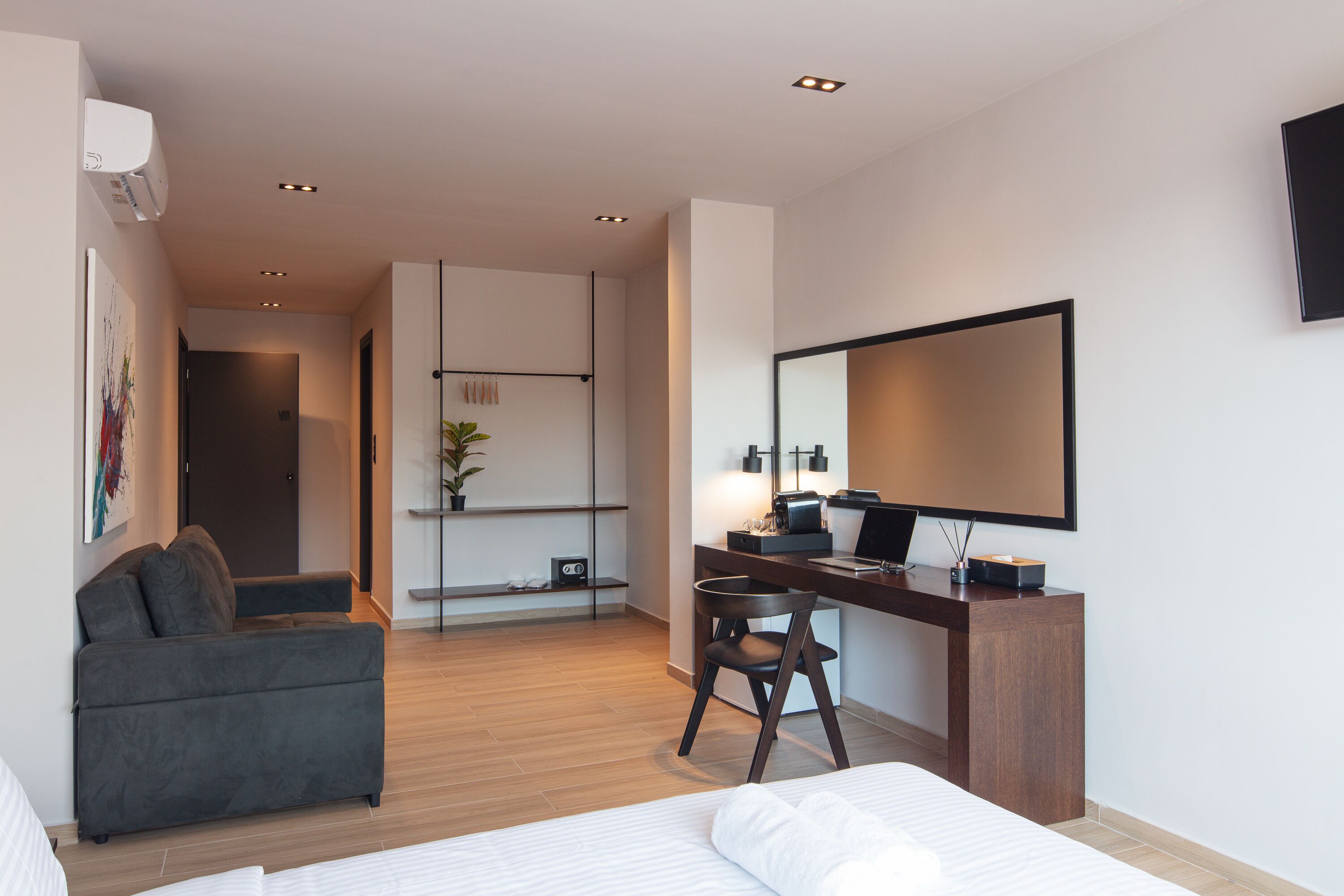 A modern hotel room with a bed, a desk with a chair, a sofa, and a large mirror.