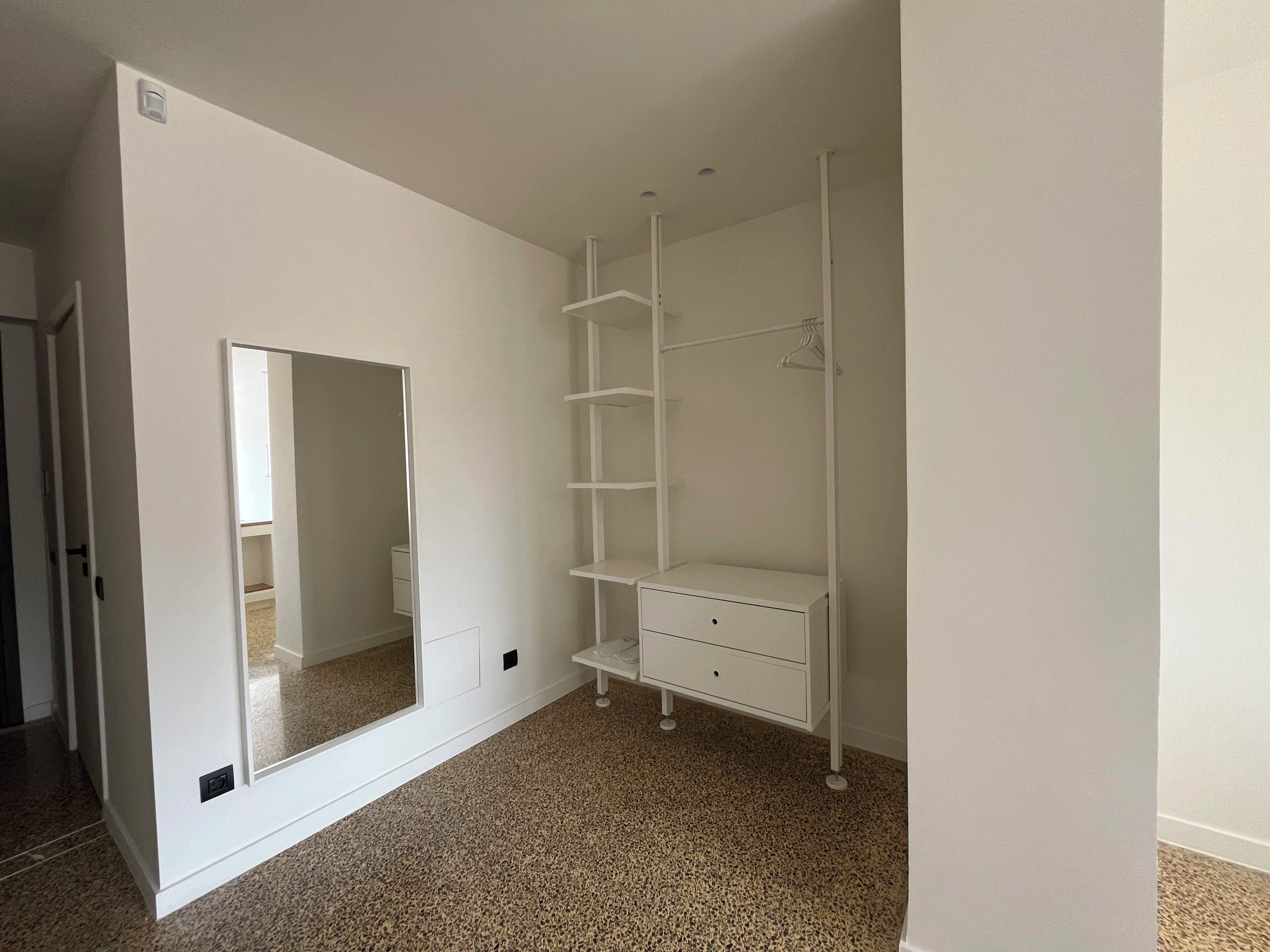 A room with a white wardrobe, a mirror, and a carpeted floor.