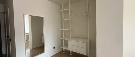 A room with a white wardrobe, a mirror, and a carpeted floor.