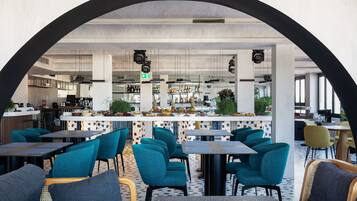 Ein modernes Restaurant mit Barbereich, petrolfarbenen Stühlen und einem gemusterten Boden.