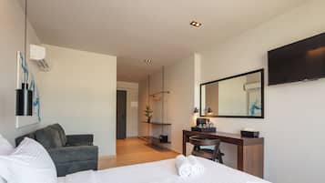 A modern hotel room with a large bed, a desk, a chair, a sofa, a flat-screen TV, and a mirror.