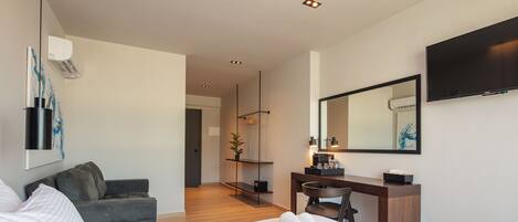 A modern hotel room with a large bed, a desk, a chair, a sofa, a flat-screen TV, and a mirror.