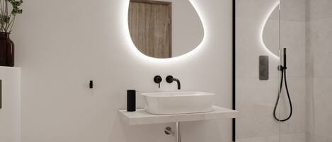 A modern bathroom with a white sink, a round mirror, a shower, and a small stool.