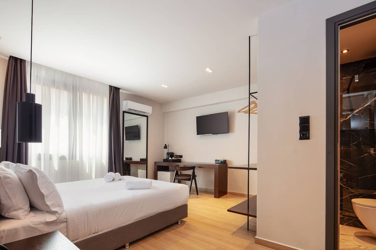 A modern hotel room with a large bed, a desk, a chair, a flat-screen TV, and a bathroom with a marble sink.