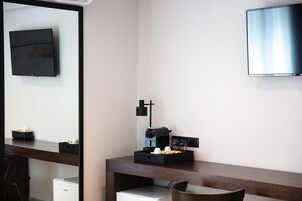 A hotel room with a desk, a coffee machine, a TV, and a mirror.