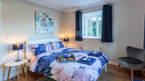 A bedroom with a bed, a side table, a chair, a window with curtains, and a painting on the wall.