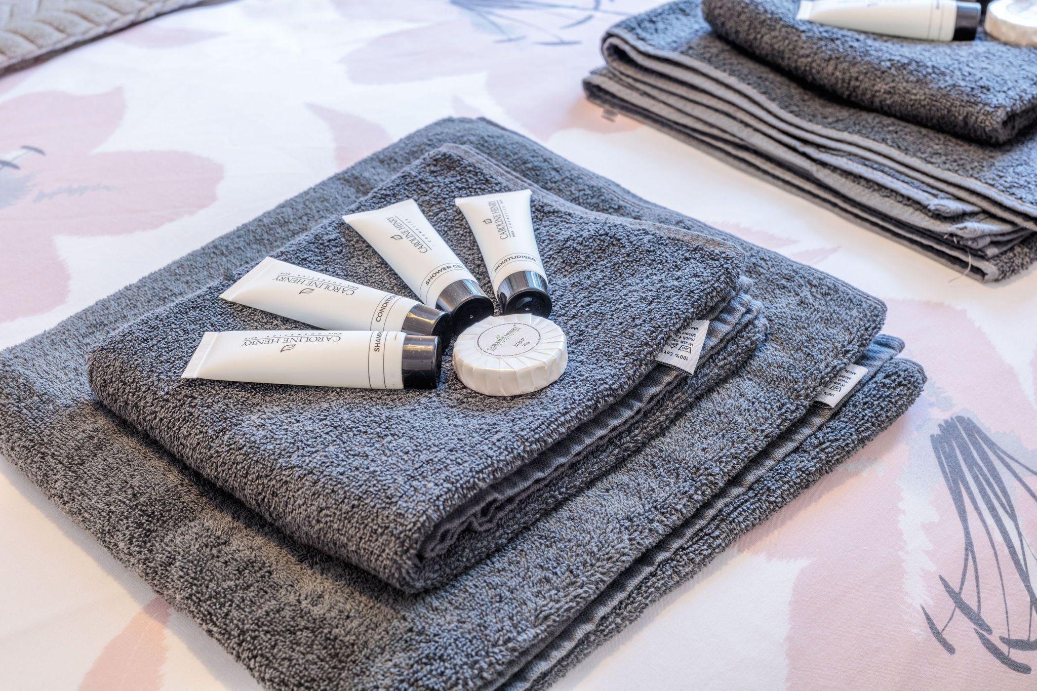 A neatly arranged set of towels and toiletries on a bed with a floral bedspread.