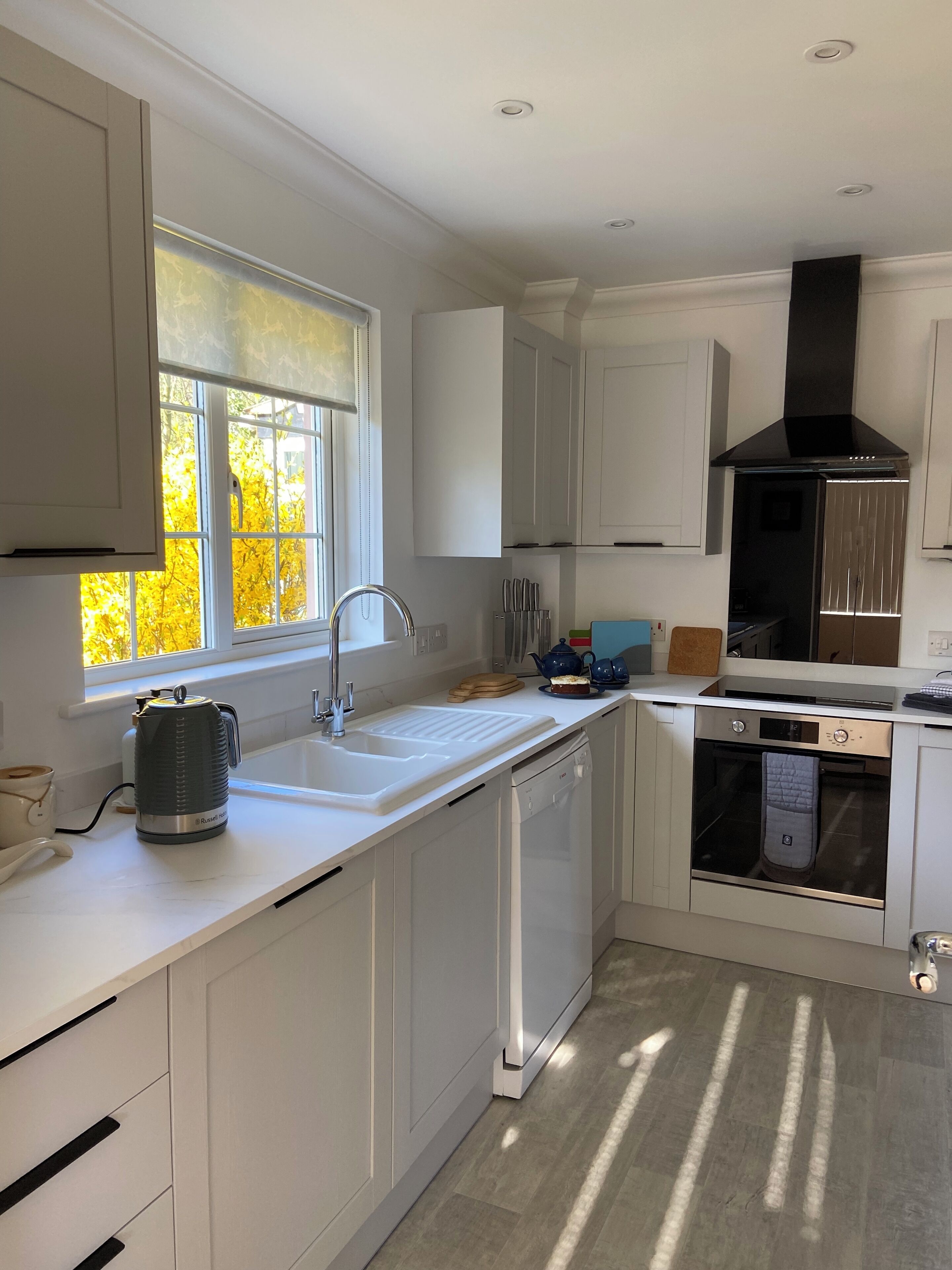 A modern kitchen with white cabinetry, a built-in oven, and a window with a view of autumn trees.