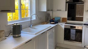 A modern kitchen with white cabinetry, a built-in oven, and a window with a view of autumn trees.