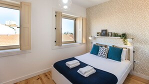 A bedroom with a bed, two windows, a headboard, and a wall with a leaf pattern.