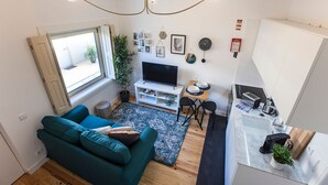 A compact living space with a teal sofa, a TV, a dining area, and a kitchenette.