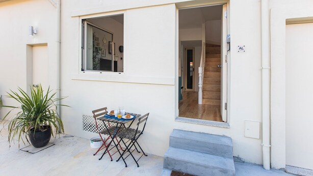 A small outdoor dining area with a table and chairs, a potted plant, and a staircase leading to an interior room.