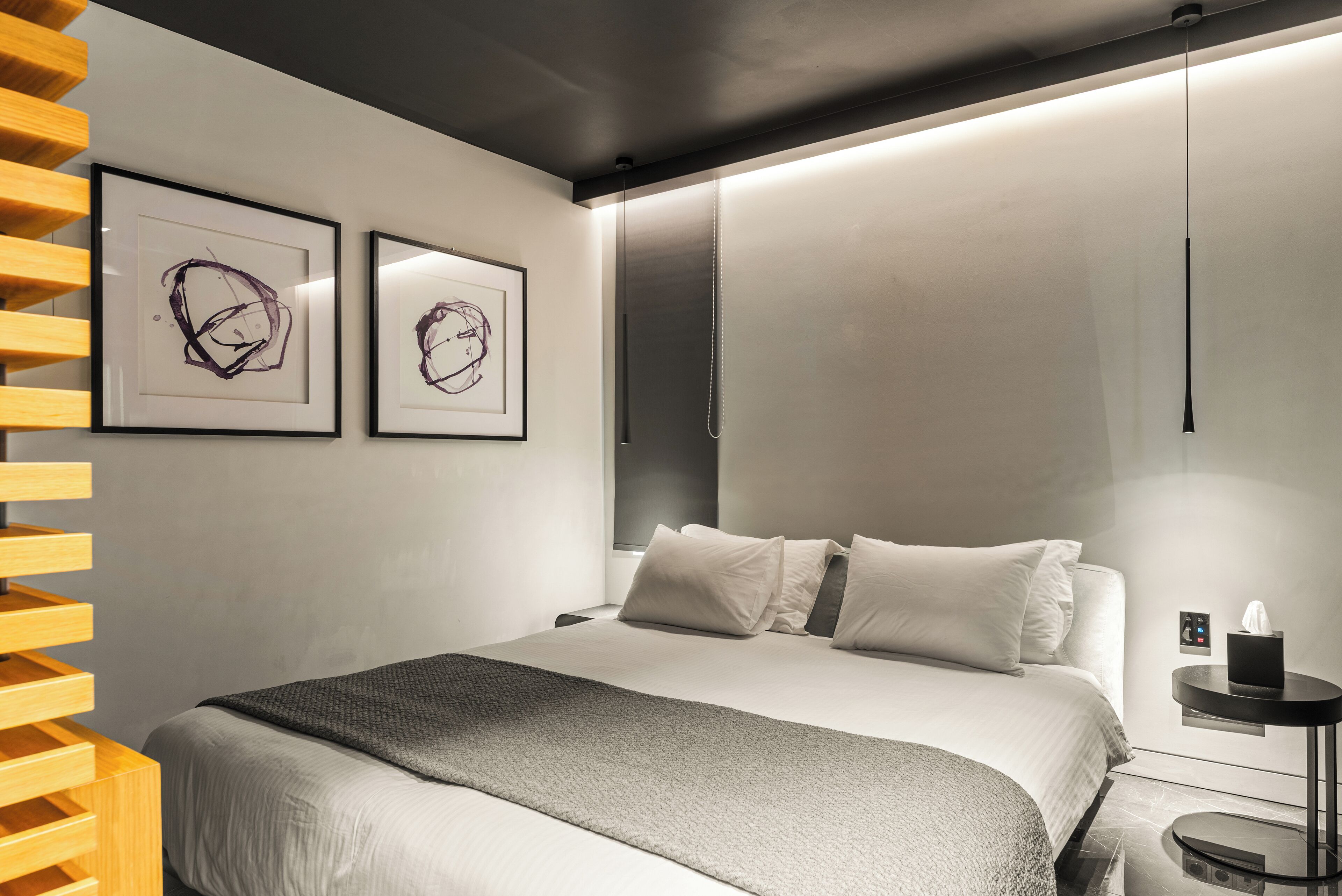 A modern bedroom with a bed, a bedside table, and two framed abstract artworks on the wall.