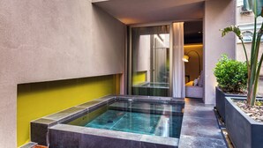 Uma área de spa moderna ao ar livre, com hidromassagem, espaço de estar com almofadas e um vaso de planta.