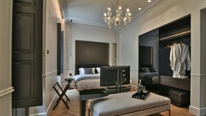 Quarto moderno com cama grande, TV, um banquinho e um cabideiro.