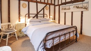 A bedroom with a metal bed frame, a white chair, a nightstand with a lamp, and a painting on the wall.