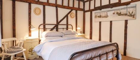 A bedroom with a metal bed frame, a white chair, a nightstand with a lamp, and a painting on the wall.