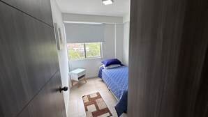 A small bedroom with a bed, a nightstand, a window, and a door.