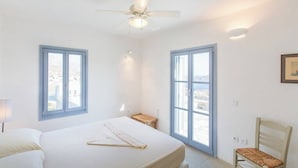 A bedroom with a bed, a ceiling fan, two windows, a chair, and a small table.