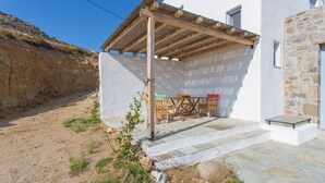 A white building with a stone facade, a wooden pergola, and a stone staircase leading to a door.