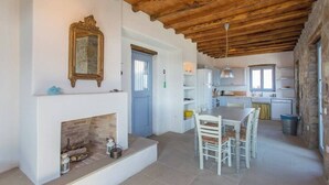 A spacious kitchen with a fireplace, wooden ceiling, and a dining area with white furniture.