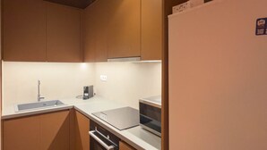 A compact kitchen with wooden cabinets, a stainless steel sink, a built-in oven, and a white refrigerator. - Elegant Retreat in Kolonaki - Renovated April 2026 (Athens)