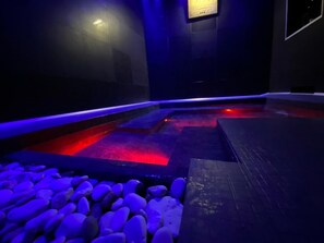 A dimly lit indoor pool area with blue lighting, stone steps, and a plaque on the wall. - Residenze Romano Albergo diffuso & spa (Foggia)