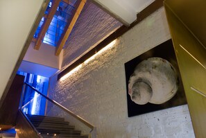 A staircase with wooden railings leading to a lower level, a textured brick wall, and a large spherical object mounted on the wall. - Residenze Romano Albergo diffuso & spa (Foggia)