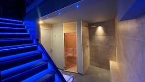 A modern bathroom with a shower, a wooden door, and a blue-lit staircase. - Residenze Romano Albergo diffuso & spa (Foggia)