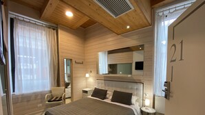 A bedroom with a large bed, a bedside table, a chair, a mirror, and a window with curtains. - Residenze Romano Albergo diffuso & spa (Foggia)