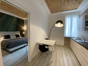 A compact room with a bed, a desk, a chair, a lamp, and a kitchenette. - Residenze Romano Albergo diffuso & spa (Foggia)