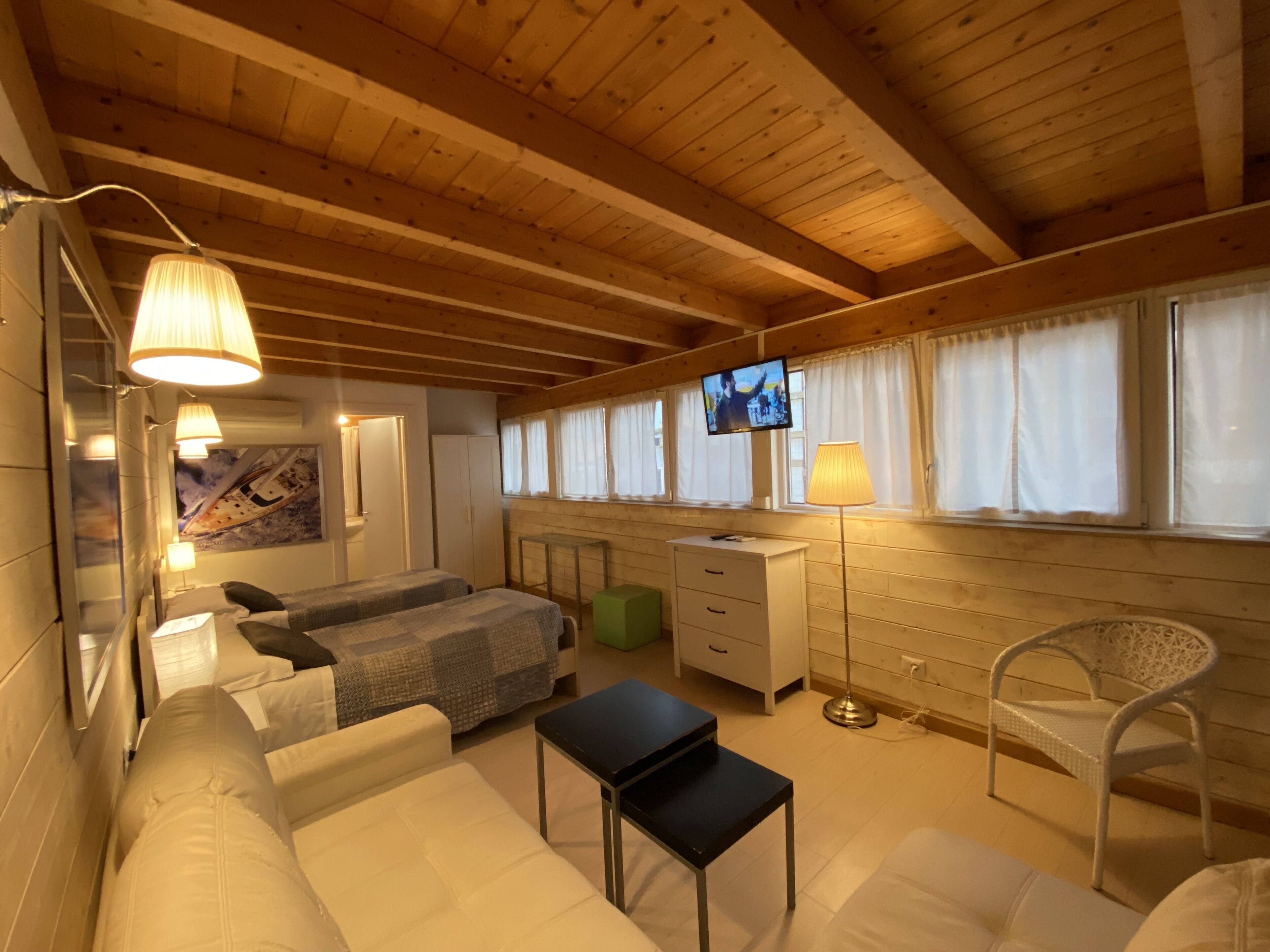 A cozy room with wooden beams, a bed, a sofa, a desk, and a TV.