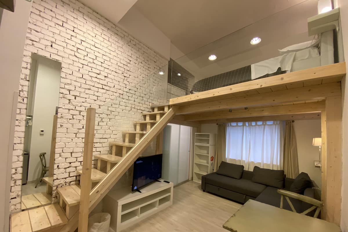 A modern living space with a brick wall, wooden staircase, flat-screen TV, sofa, and a table.