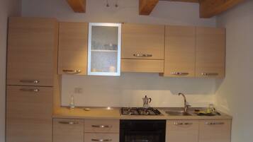 Una cucina compatta con mobili in legno, forno a incasso, lavello e una finestra sopra il piano di lavoro.