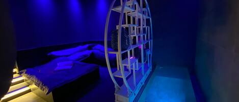 A room with a bed, a massage table, and a unique spherical structure with shelves.