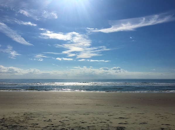 Una playa con cielo despejado y el sol reflejándose en el agua.