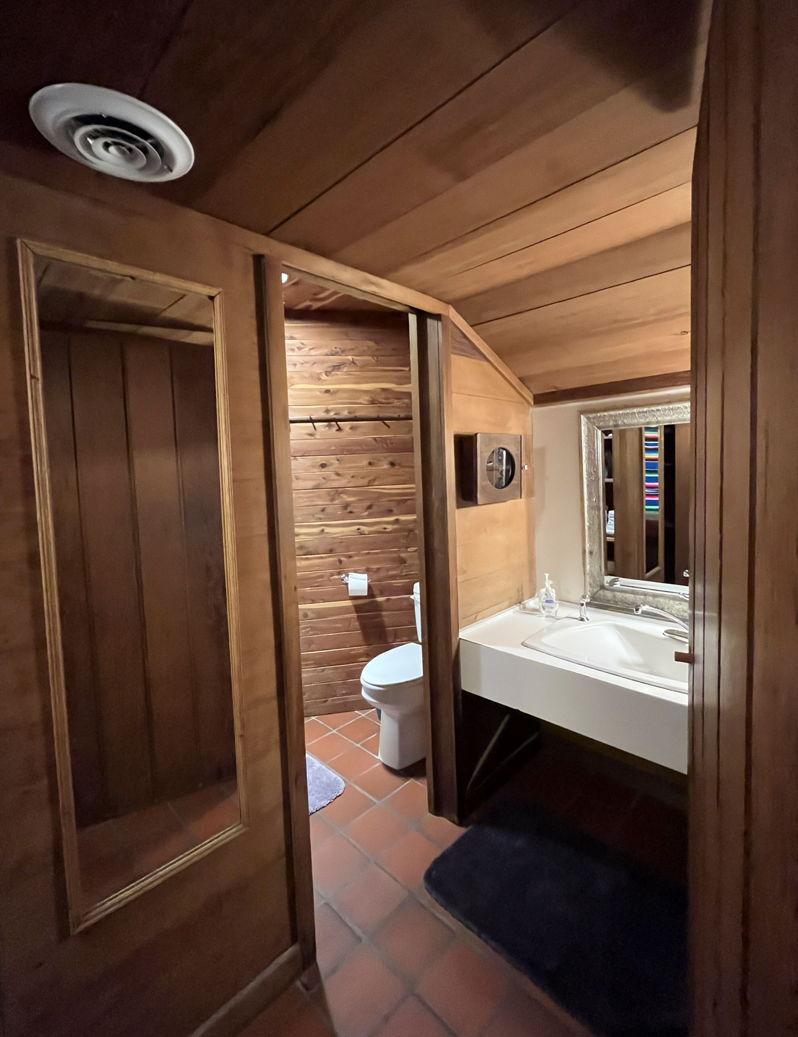 A wooden interior with a bathroom featuring a toilet, sink, and mirror.