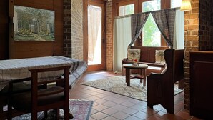 Una habitación acogedora con una cama de madera, un banco, una mesita con un florero y un ventanal con cortinas.