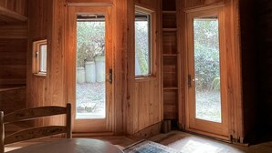 Una cabaña de madera con dos puertas grandes, un ventanal pequeño y una mesa con sillas.