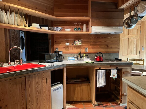 A compact kitchen with wooden cabinetry, a built-in oven, a coffee maker, and a kettle.