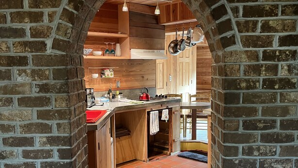 Una cocina con un arco de ladrillo, armarios de madera, suelo de baldosas y ollas colgantes.