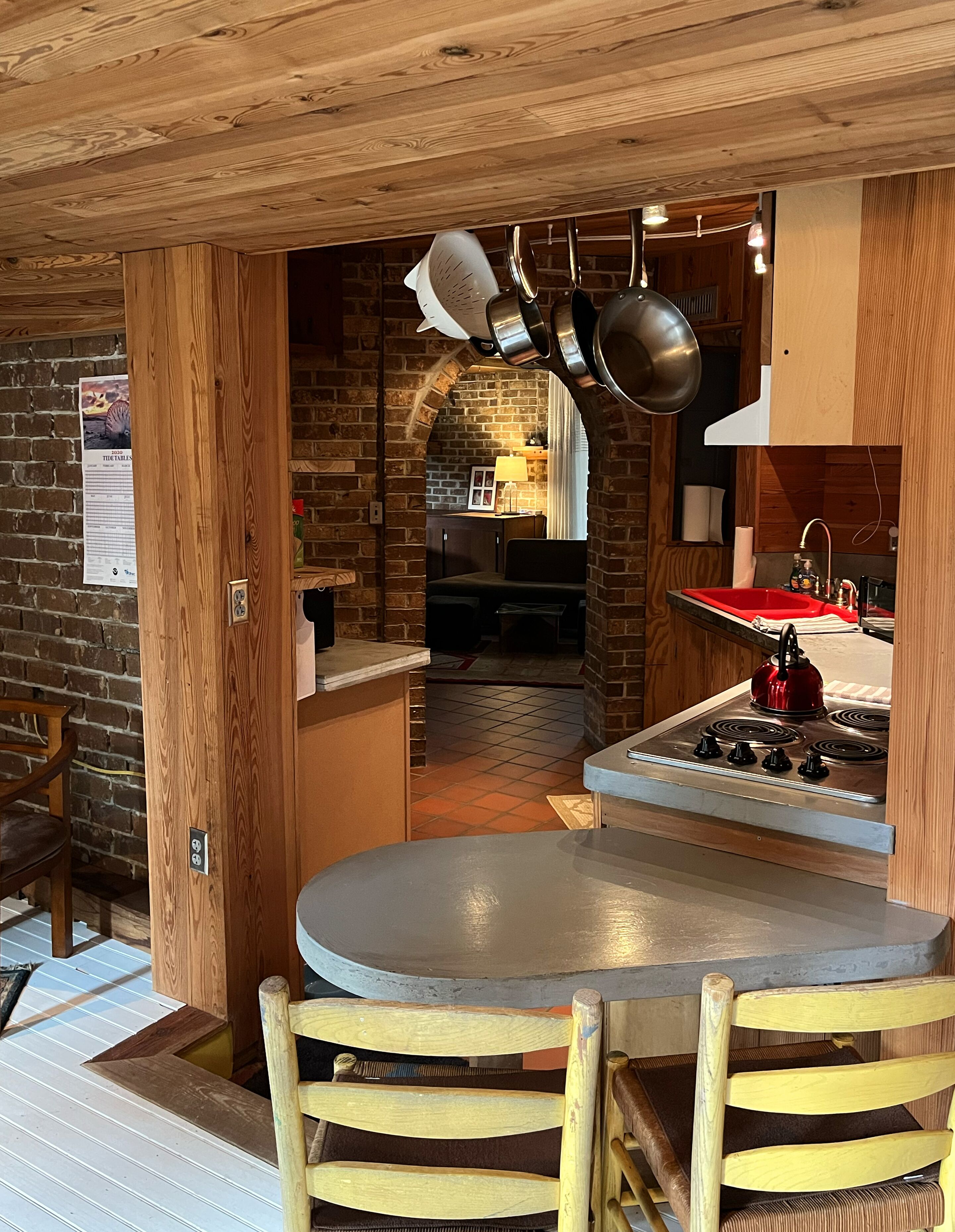 Une cuisine rustique avec un plafond en bois, un évier rouge et des casseroles suspendues.