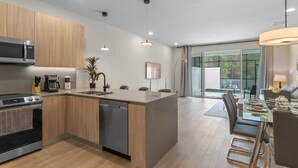 A modern kitchen with wooden cabinets, a built-in oven, a microwave, and a dishwasher. There is a dining area with a table and chairs, and a large window providing a view of the outdoors. - Amazing NEW pool house near Disney (Clermont)