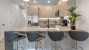 A modern kitchen with a central island, stainless steel appliances, and bar stools. - Amazing NEW pool house near Disney (Clermont)