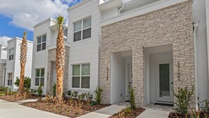 A modern residential building with white exterior walls, stone accents, and a well-maintained front yard with palm trees and shrubs. - Amazing NEW pool house near Disney (Clermont)