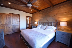 A wooden-paneled bedroom with a large bed, two bedside tables, and a ceiling fan.
