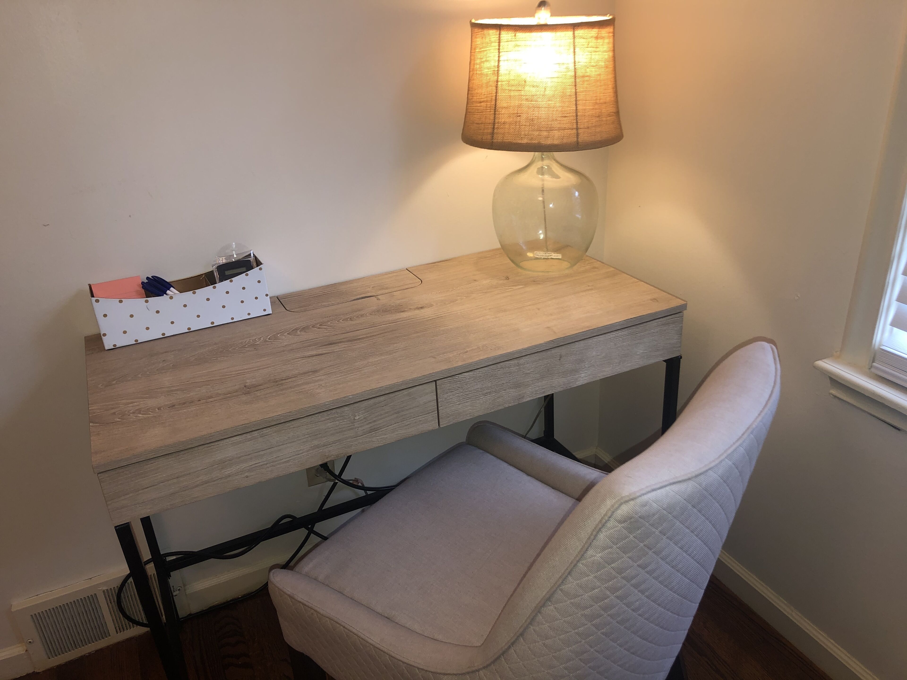 Ein Arbeitsplatz mit einem Holztisch, einer Lampe, einer Aufbewahrungsbox mit Punkten und einem gepolsterten Stuhl.