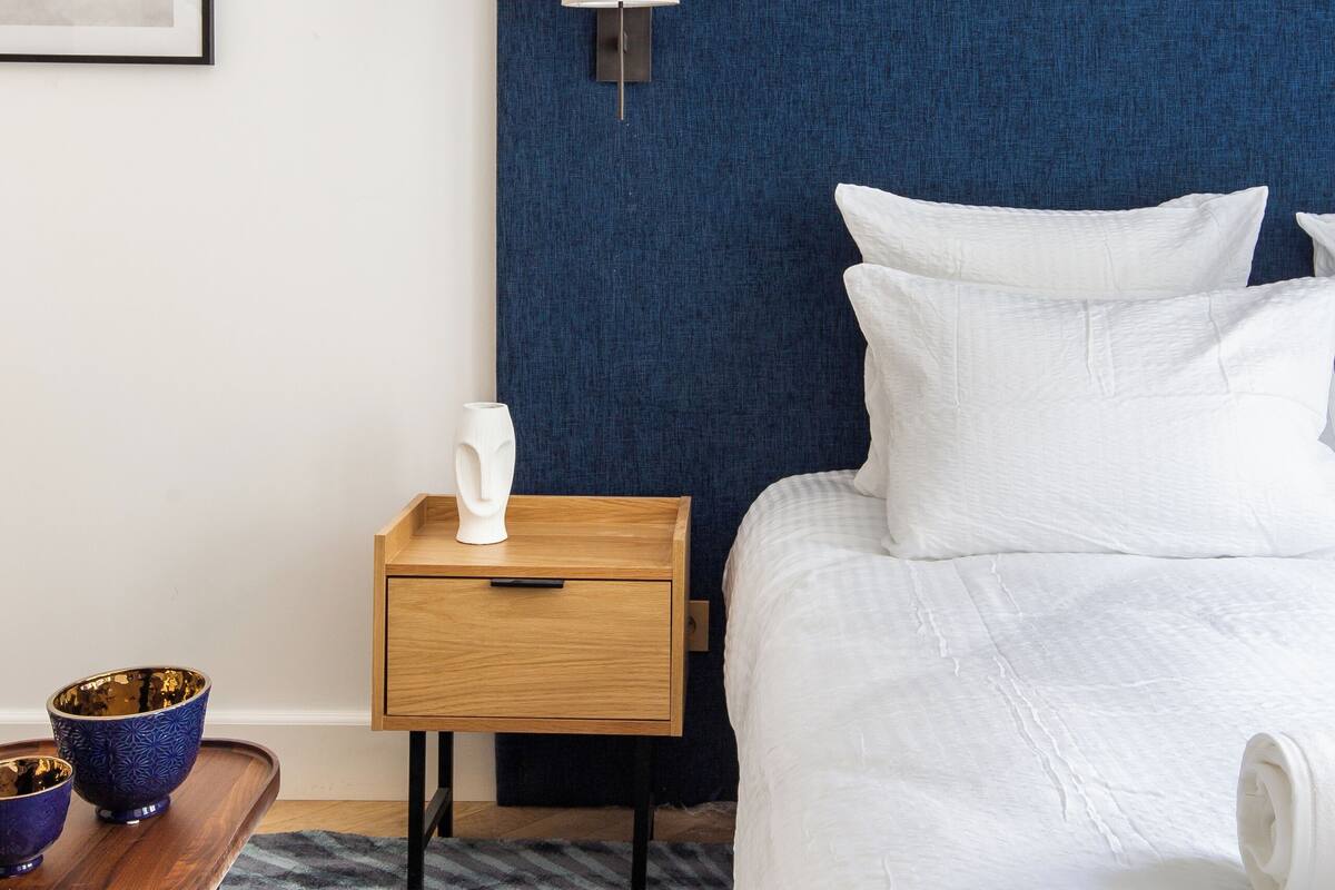 A neatly arranged hotel room with a bed, bedside table, lamp, and a framed artwork on the wall.