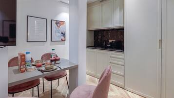 Una cocina moderna con armarios blancos, encimera de mármol y un comedor con sillas rosadas y una mesa dispuesta para dos personas.