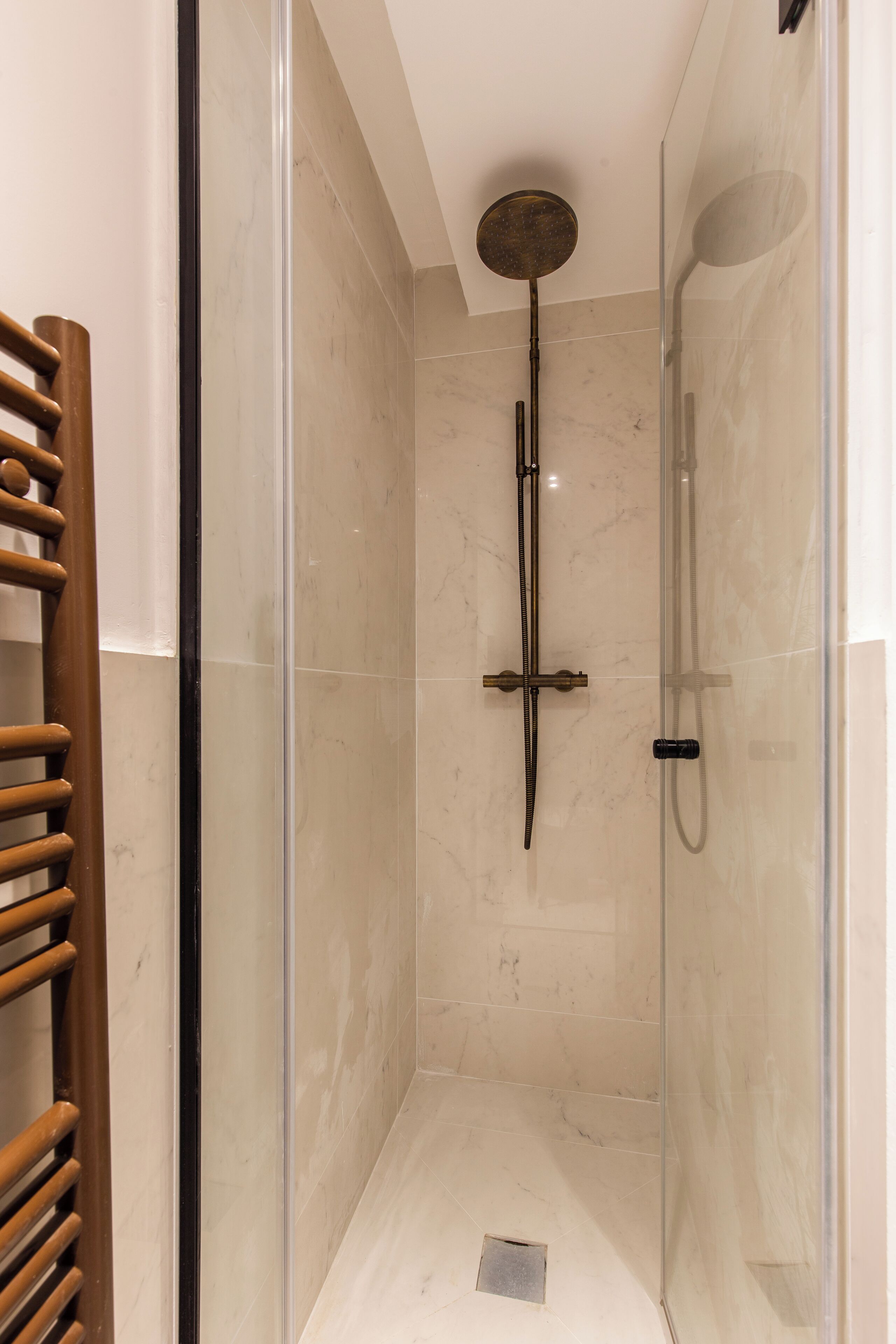 A glass-enclosed shower stall with a handheld showerhead and a wall-mounted faucet.